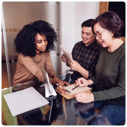 Three colleagues in an office reviewing a document and smiling — representing teamwork and professional HR support.