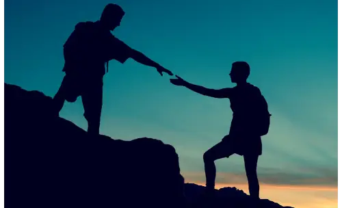 Two climbers silhouetted on a mountain, one assisting the other — representing collaboration, support, and teamwork.