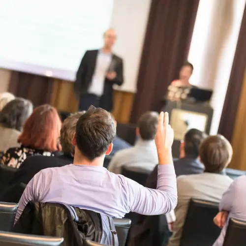 Audience in a lecture theatre with hands raised during a training session — illustrating active learning and professional development.