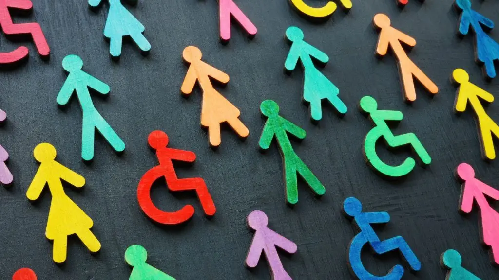 Wooden cut-outs of people in various colours on a blackboard — representing men, women, and disabled individuals, symbolising diversity and inclusion.